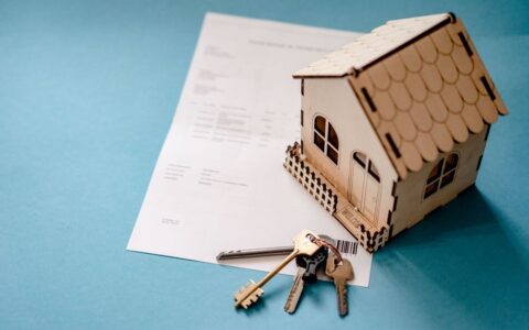Miniature wooden house with keys and contract symbolizing real estate transactions.