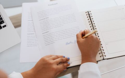Close-up of hands signing a contract on a desk with office supplies, symbolizing legal agreements.