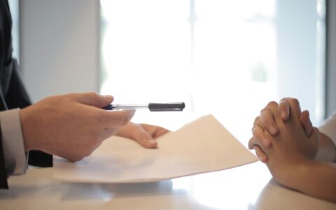 Side view of faceless formal man giving pen and paper to focused female with clenched hands at table on meeting