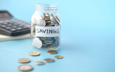 Glass jar labeled 'Savings' filled with coins, beside a calculator on a blue background.