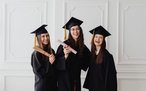 Three happy female graduates in caps and gowns holding diplomas and celebrating their achievement.