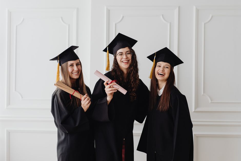 Three happy female graduates in caps and gowns holding diplomas and celebrating their achievement.
