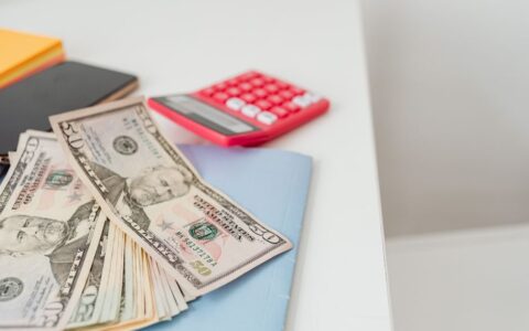 Close-up of notebooks, US dollars, and a calculator on a desk.