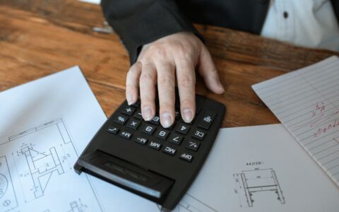 Hand using calculator for architectural calculations on blueprints.