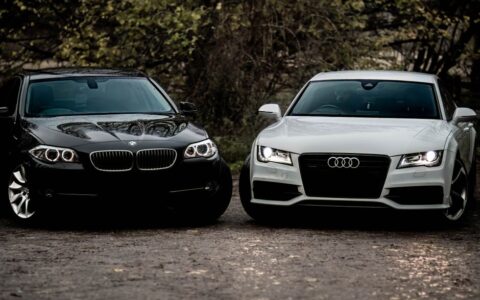 Black BMW and white Audi luxury sedans parked outdoors on a gravel path.