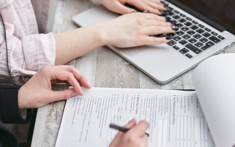 Close-up of hands typing on a laptop and reviewing business documents, focused on finance and legal tasks.